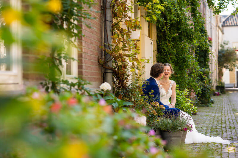 Trouwfotograaf Den Bosch - bruidspaar op bankje tussen de bloemen in oud straatje in Den Bosch